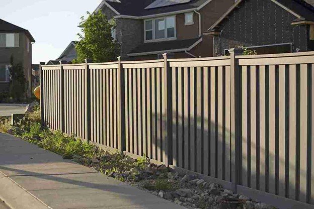 Long beige privacy fence installed along a sidewalk in a suburban neighborhood with homes visible in the background.