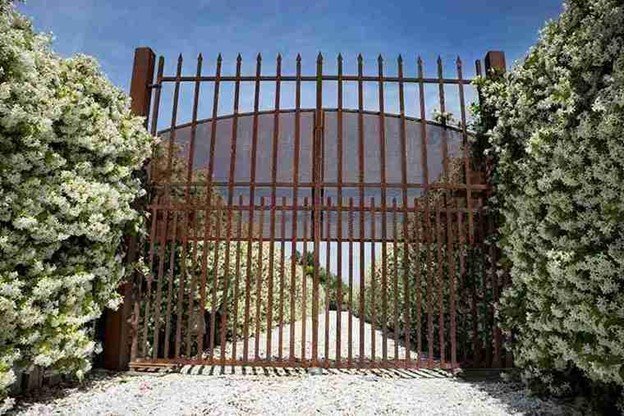 Rusted metal driveway gate removed and replaced with a secure residential gate framed by landscaped hedges.