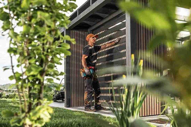 Fence repair technician inspecting and adjusting modern wood fence panels during a residential fence repair project.