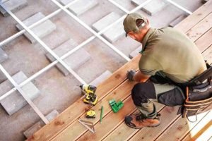Contractor installing wooden deck boards using power tools and measuring equipment