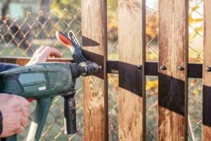 Hand holding a power drill while repairing a wooden fence panel