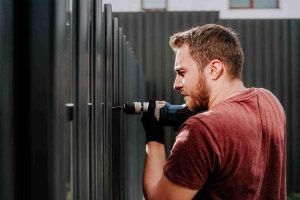 Man using a power drill to install vertical metal slats on a sliding gate